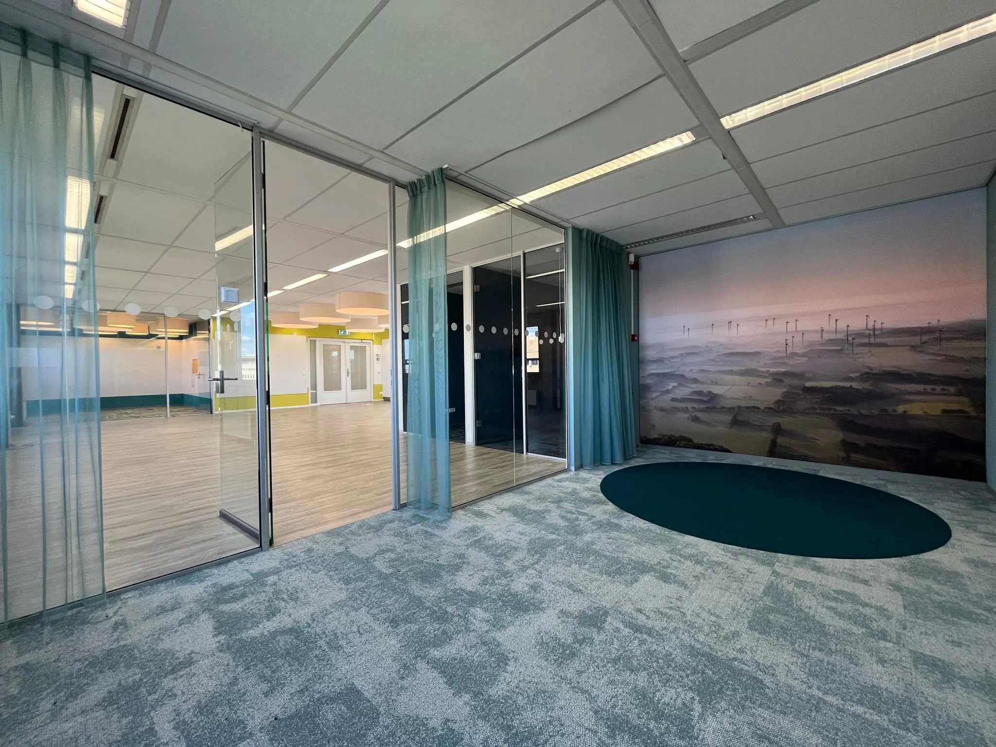 Moderne kantoorruimte aan de Barchman Wuytierslaan met glazen wanden, licht houten vloer, blauwe accenten en een muurdecoratie van een windmolenlandschap.